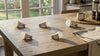 Five LED light bulbs are scattered on a sunlit wooden table. A steaming mug and a woven coaster sit nearby, creating a cozy, inviting atmosphere.