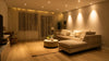 Modern living room with a beige sectional sofa, round coffee table, and potted plant. Warm lighting and sheer curtains create a cozy, inviting atmosphere.